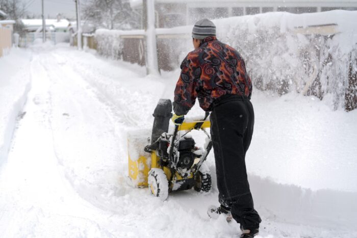 Mężczyzna usuwa śnieg z podwórka;